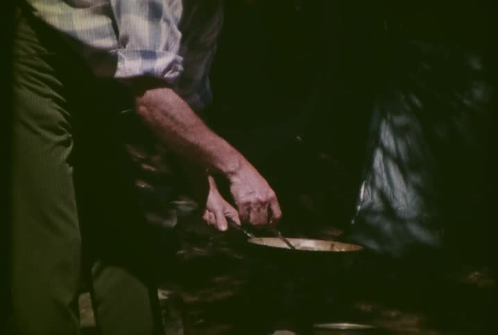 A man is cooking in a pan by a campfire