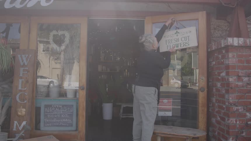 Woman hangs a fresh cut flowers sign on the entrance door of a flower shop