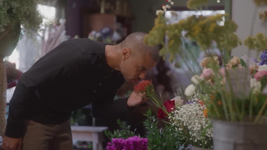 Man smells a flower among various arrangements in a flower shop