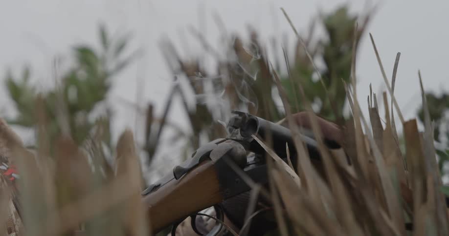 A male hunter in the jungle prepares his gun after taking a shot as smoke exits the shotgun chamber at midday