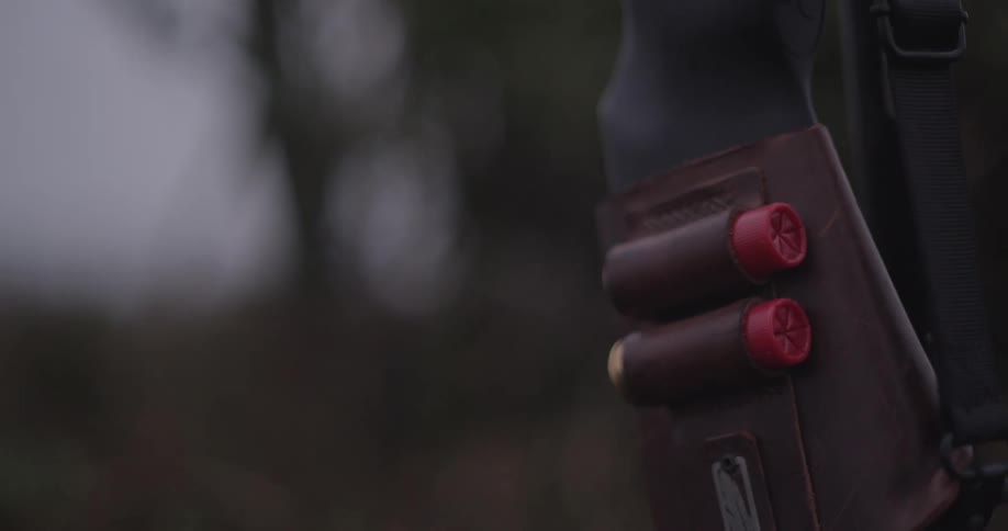 A shotgun with bullets in its casing is carried by a hunter in the jungle