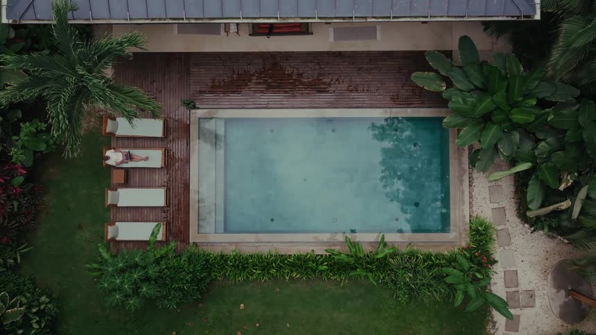 Pool surrounded by tropical greenery beside wooden lounge chairs