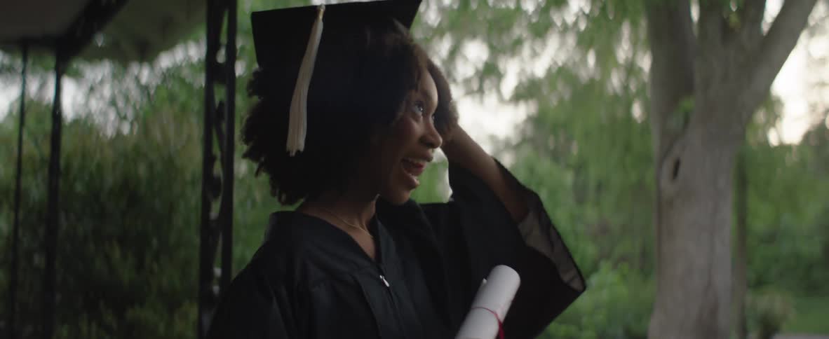 Young woman smiles while raising her graduation cap in celebration under natural light