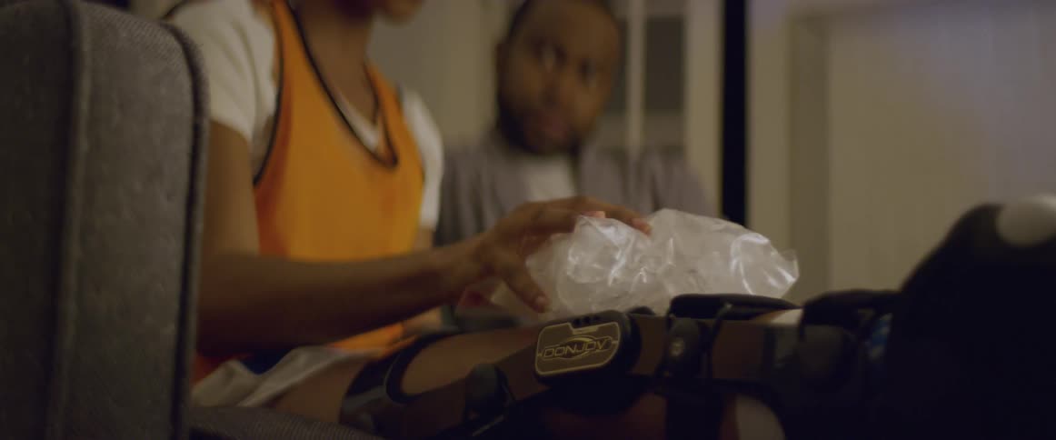 Person with an orthopedic knee brace applies an ice pack to their leg while a man watches with concern