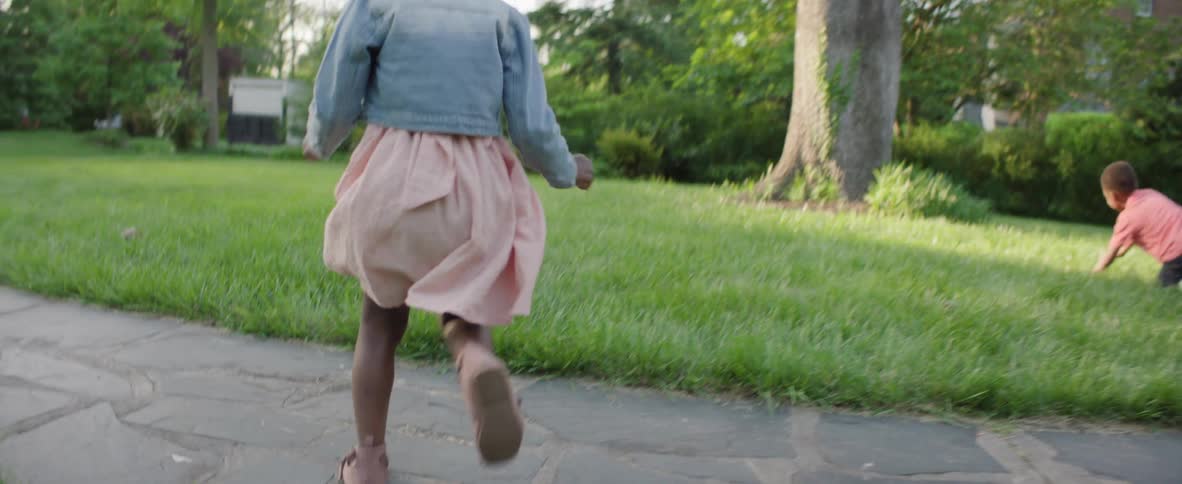Children run across the lawn in a treelined neighborhood during the afternoon