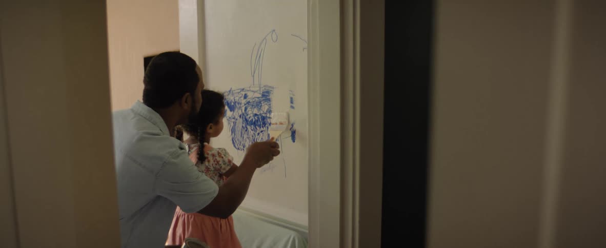 Father paints a drawing on the wall with white paint together with his little daughter inside the house