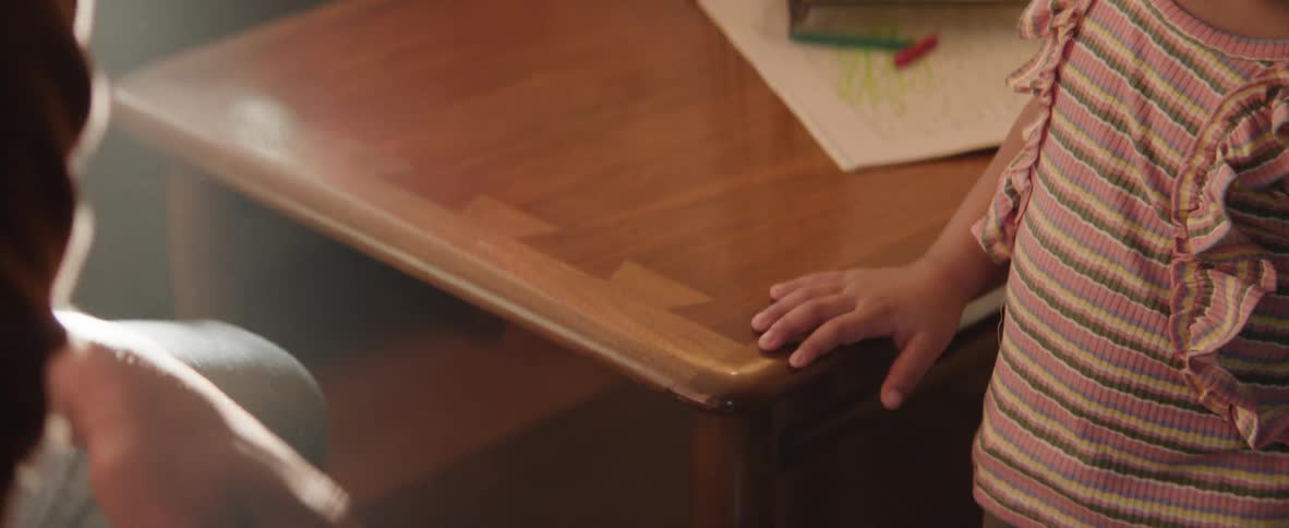 A father walks up to his daughter who is standing next to a table holding a marker