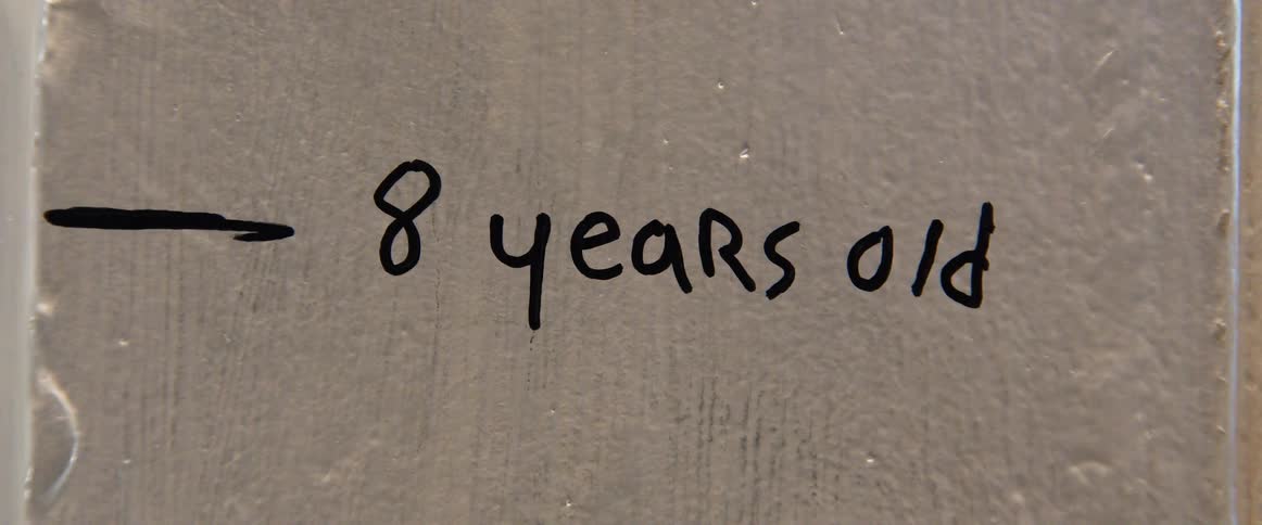 A shot of a grey wall with a note on it the text 8 years old is written in black with an arrow pointing to it
