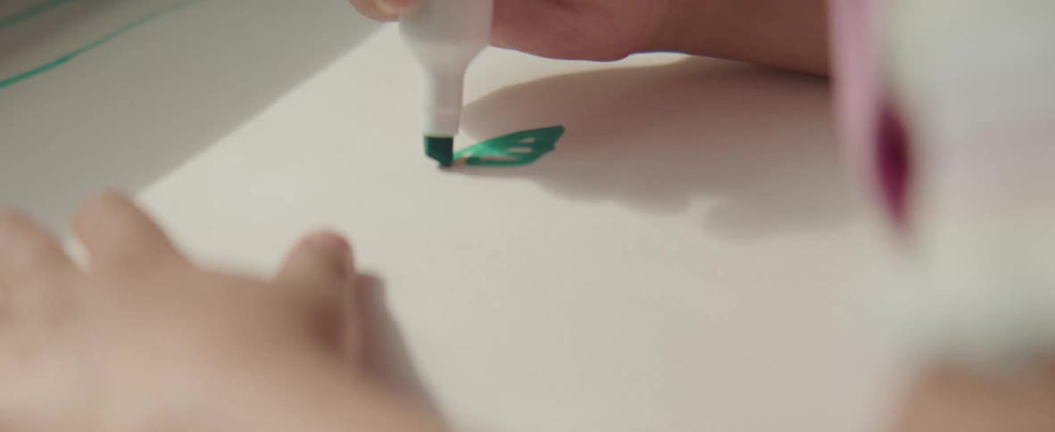 A kid uses a green marker to color on a white piece of paper