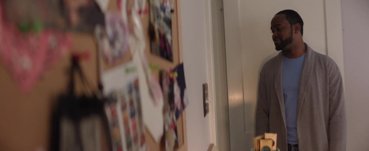 Man with a calm expression holds a tray in a home hallway decorated with a photo board