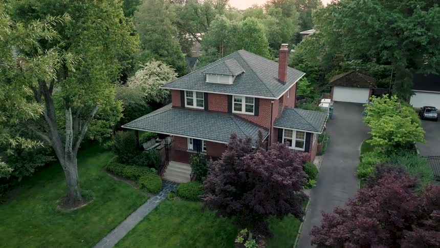 A suburban home surrounded by trees and grass in the midday sun