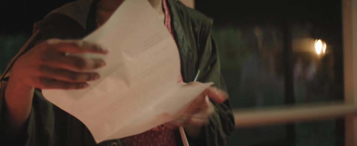 A shot of a person opening an envelope and reading a letter they cover their mouth in surprise or shock at the end of the video