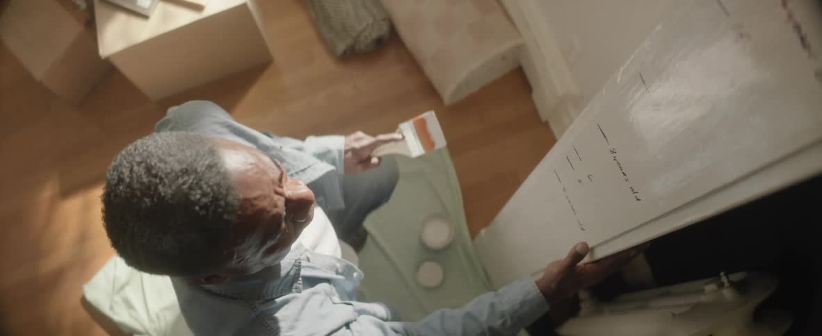 Man holding a paintbrush while painting a white surface marked with childrens height measurements