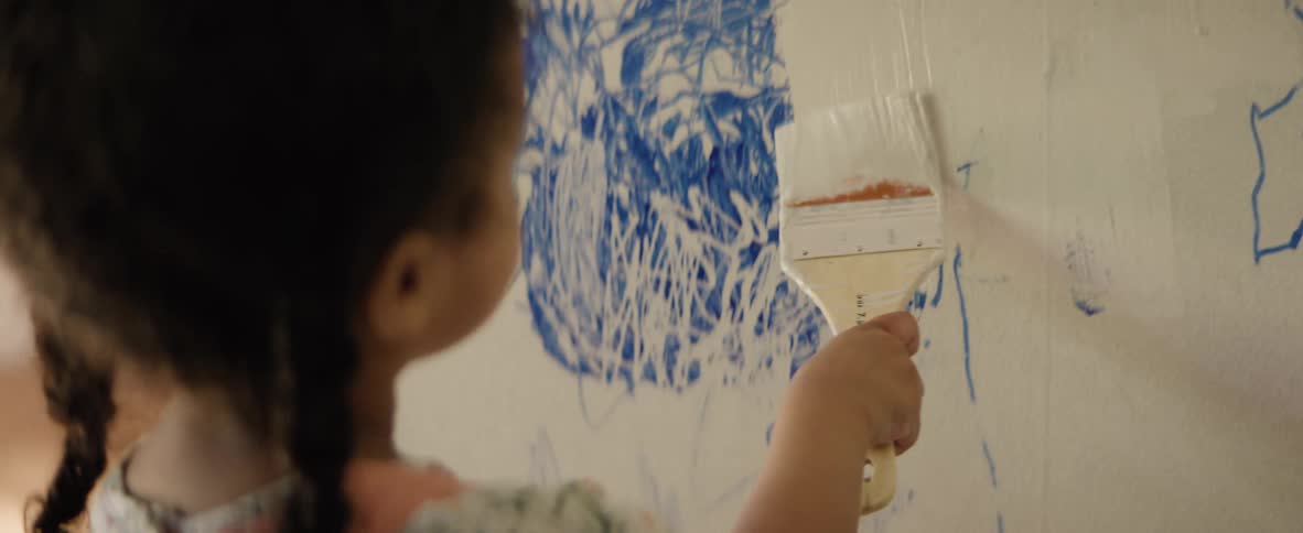 A girl paints over a drawing on the wall