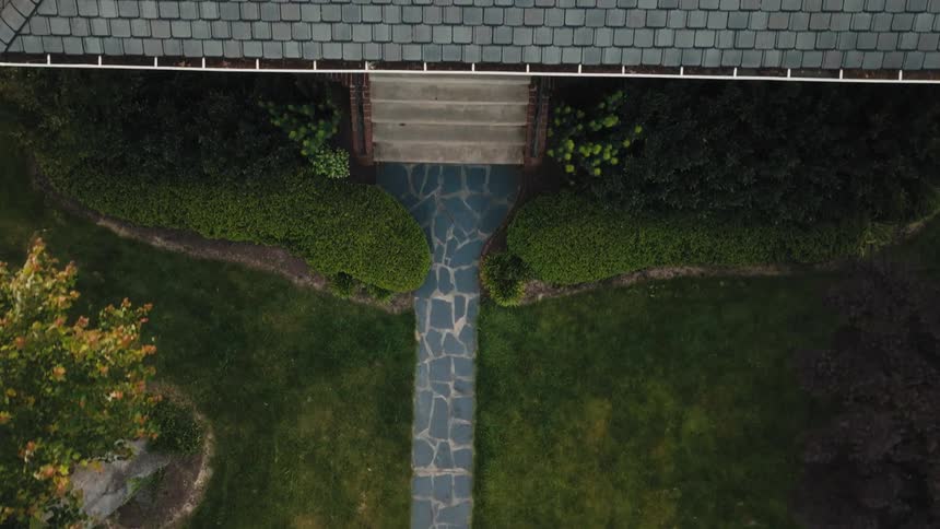 Stone pathway leading to the entrance of a house surrounded by gardens
