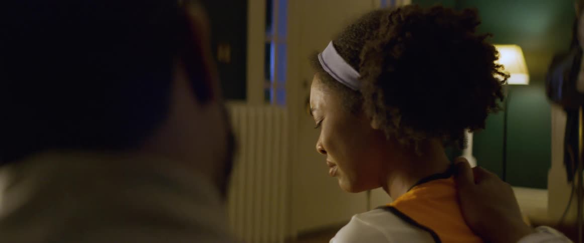 Woman with a serious expression receives a comforting hand on her shoulder from a man indoors