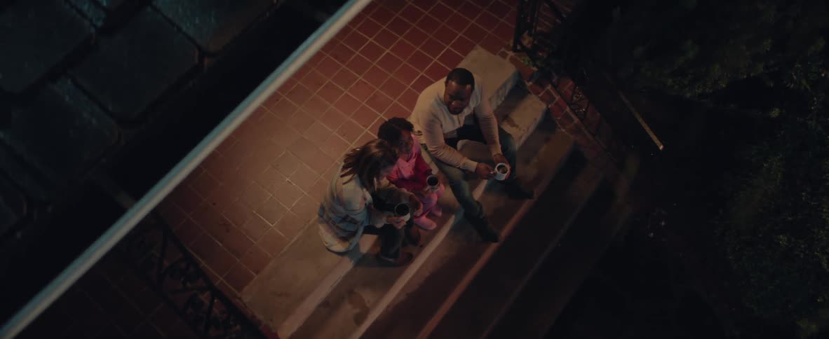 Family sitting on the outdoor steps at night holding mugs