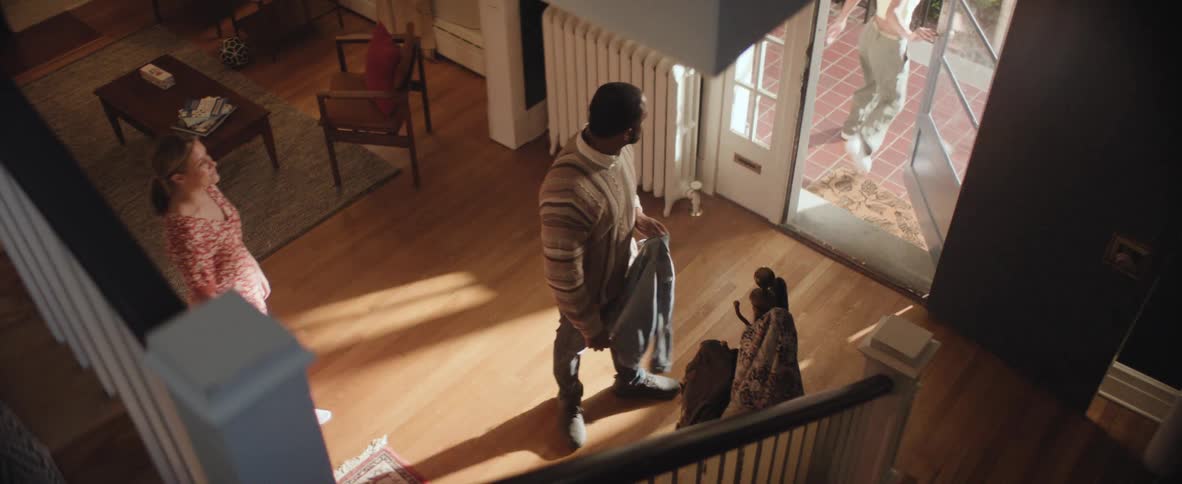 In a cozy living room a young woman walks down the stairs rejects a jacket offered by her father and walks outside then returns for the jacket after her mother embraces him