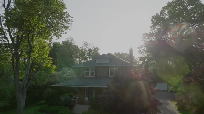 A suburban home surrounded by trees and green vegetation in spring at midday