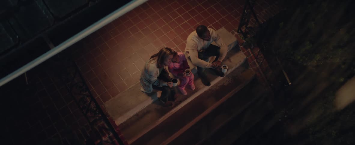 Woman man and girl sit together on the steps at night holding warm mugs in a cozy moment