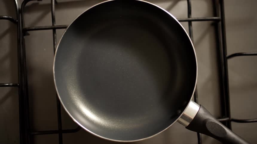 A pan is placed on a stove then an egg is cracked and added to it frying the egg