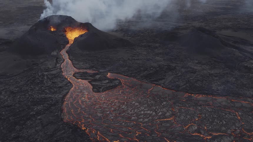 Lava flows downhill from an erupting volcano which is billowing smoke
