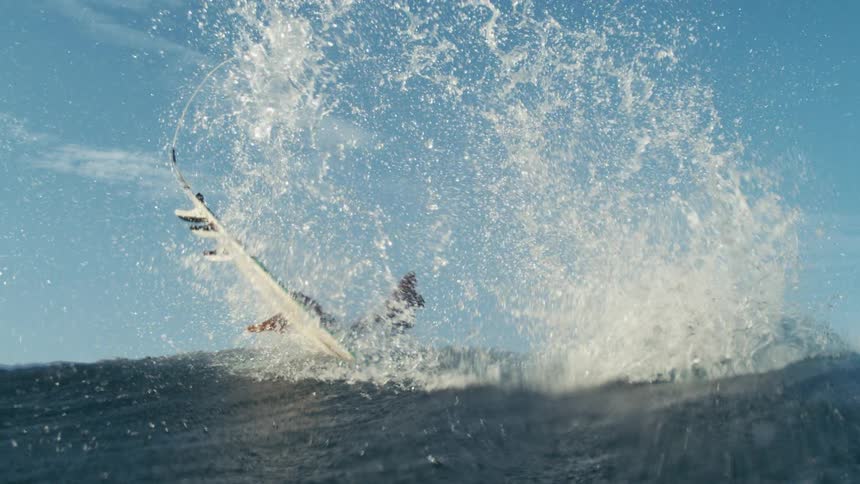 A person on a surfboard rides a gigantic wave in slow motion