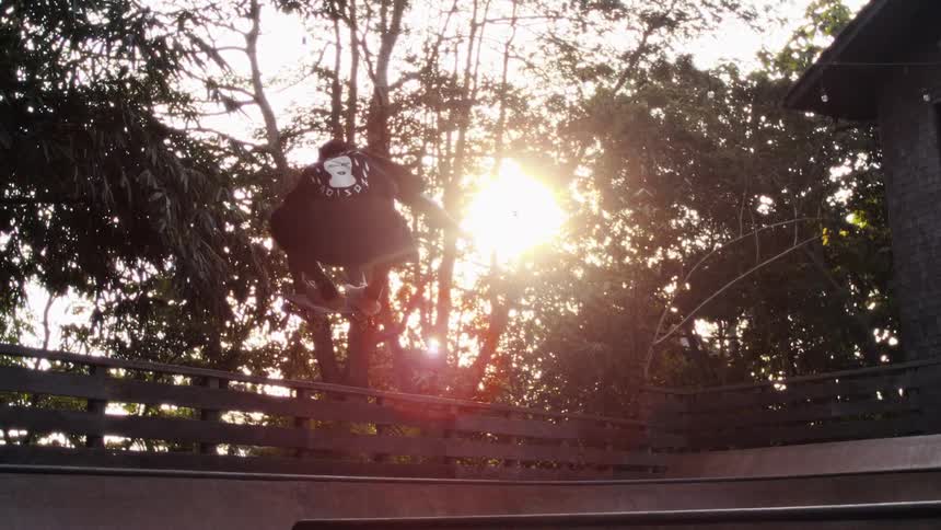 A skateboarder performs a trick over a ledge at sunset