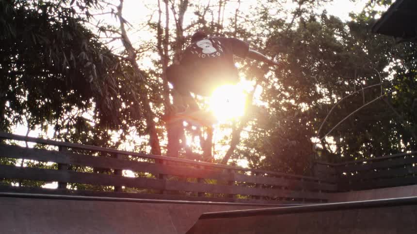 Person skateboarding on a wooden ramp at sunset with the sun shining through the trees