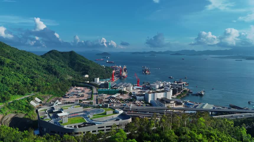 Aerial view of an industrial port surrounded by green mountains and the sea in the background