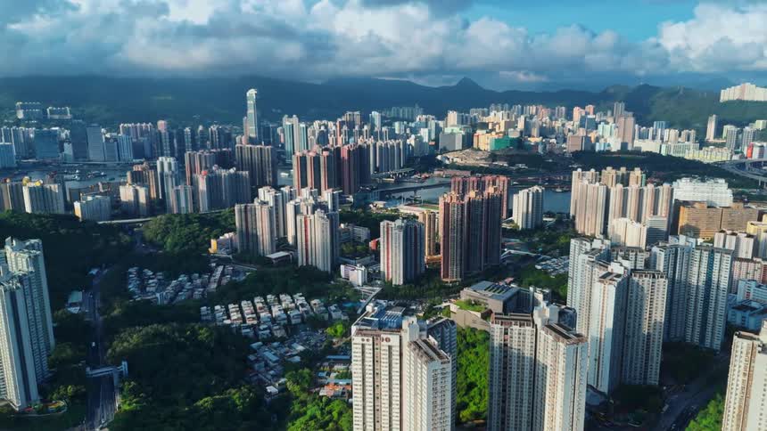 A cinematic aerial view of a sprawling cityscape with countless highrise buildings and residential towers framed by hazy mountains and a cloudy sky in the background