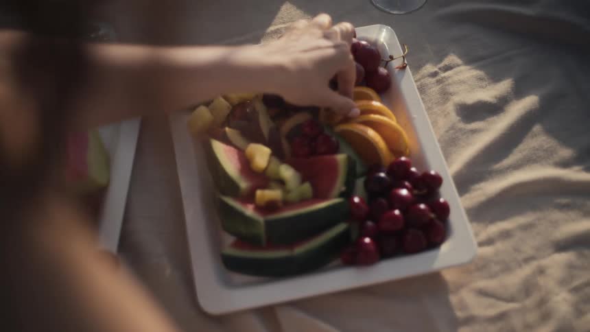 A closeup of a fruit tray featuring watermelon grapes oranges pineapple and cherries with a persons hand reaching for an orange