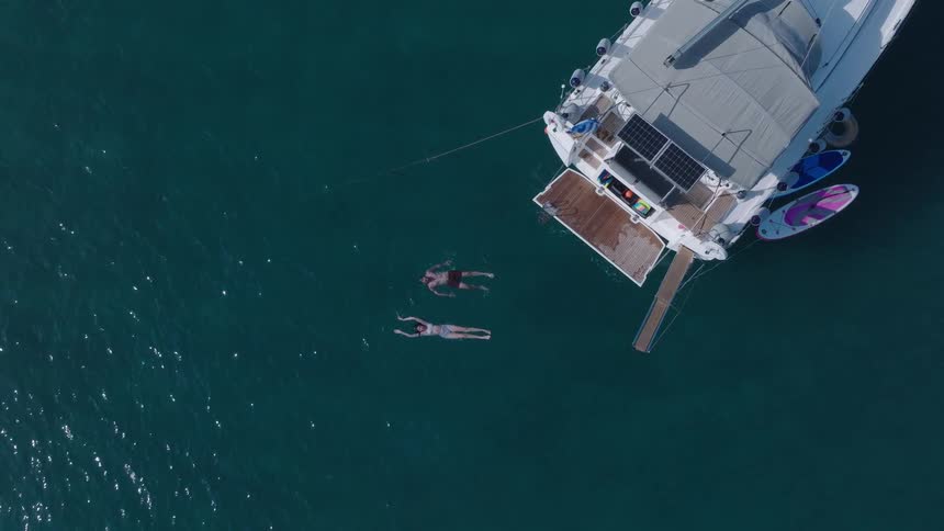 A man and a woman swim in the ocean near a yacht at midday