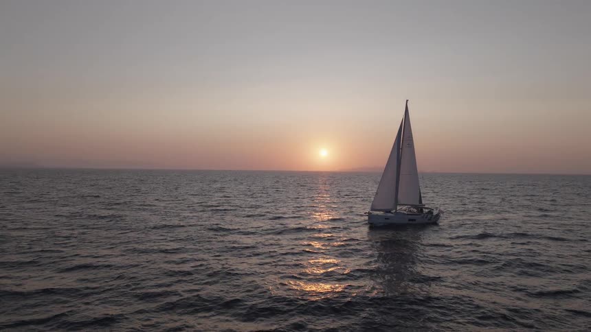 A sailboat sails across the ocean at sunset