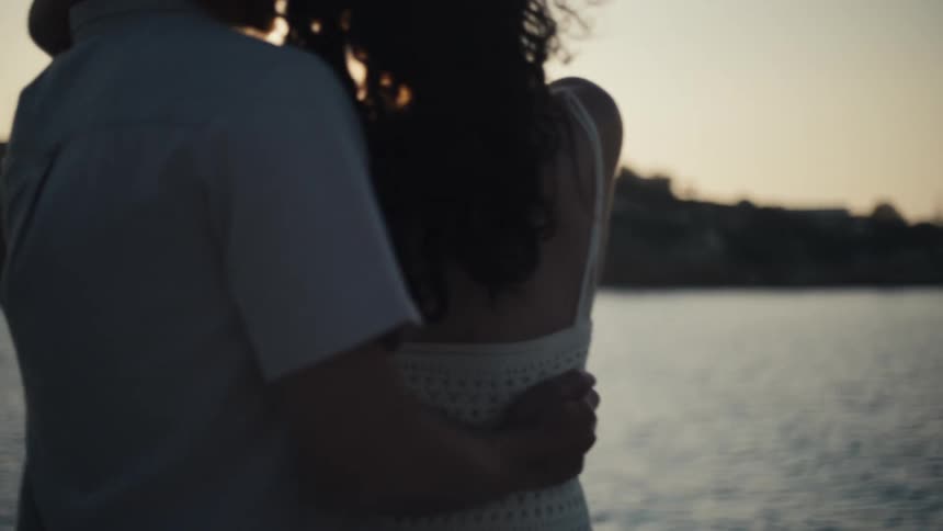 A loving couple embraces on a boat at sunset looking at each other as the womans arms are wrapped around the mans neck and his arms are around her waist