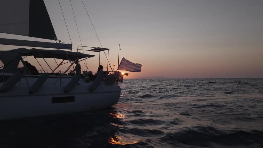 Sailboat with the greek flag sailing at sunset