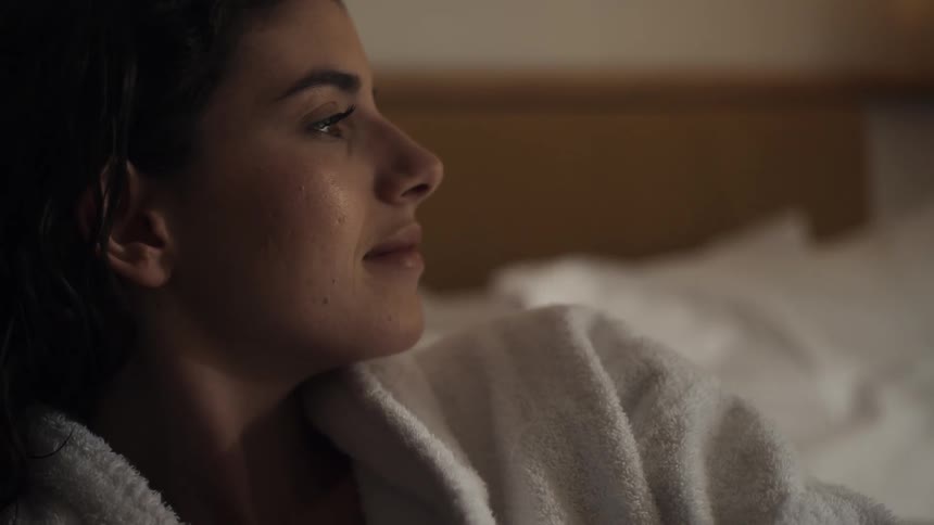 A cozy closeup sideprofile shot of a young woman lying in bed her eyes gently opening and closing as she relaxes in a brightly lit bedroom