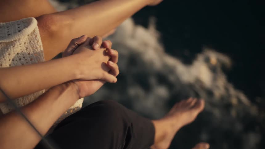 Man and woman holding hands while sitting on the edge of a boat