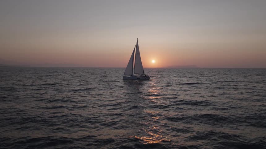 A peaceful video of a sailboat gliding across the ocean with a mesmerizing sunset or sunrise in the background