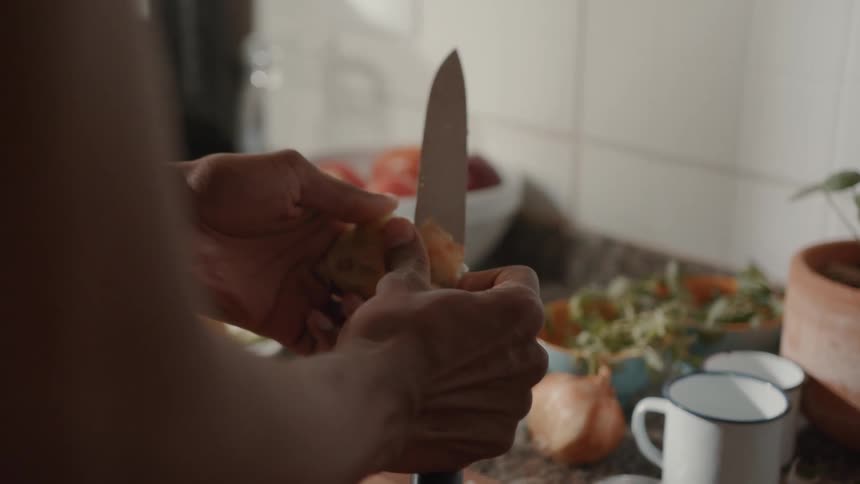 Person peeling an onion with a knife in a kitchen