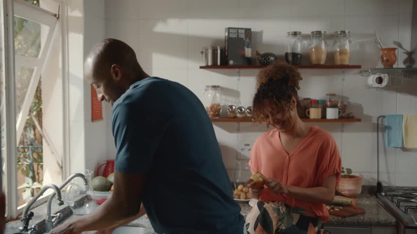 Man washing dishes and his wife peeling an apple in the kitchen