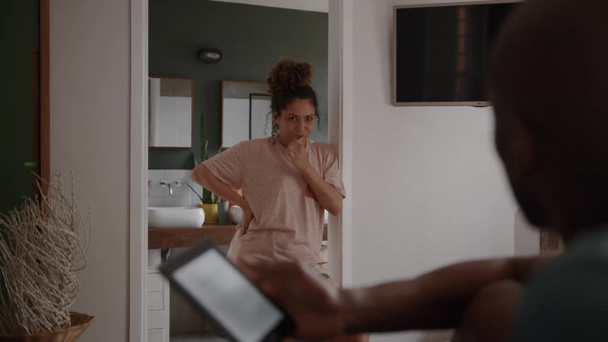 A candid moment of a couples morning routine as a woman brushes her teeth while talking to her partner