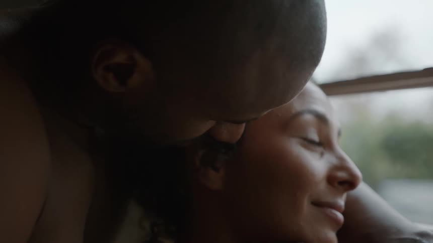 A couple is in an intimate moment with the man kissing the womans cheek the man is holding the womans chin while she looks to the side