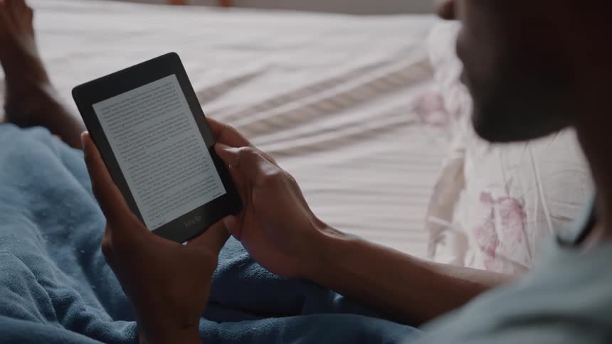 A closeup shot of a mans hands holding and reading an ebook on a tablet while relaxing in bed