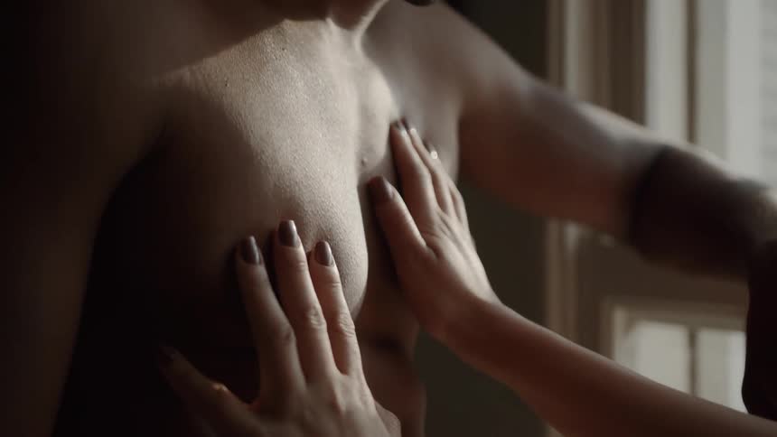 A couple is sharing an intimate moment a womans hands are caressing a mans bare chest