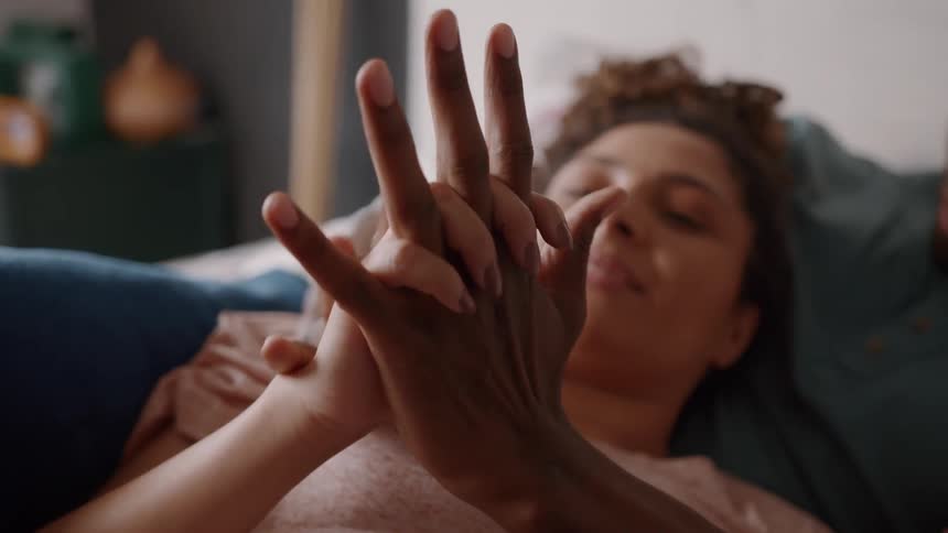 A man and woman lie together holding hands as they intertwine their fingers