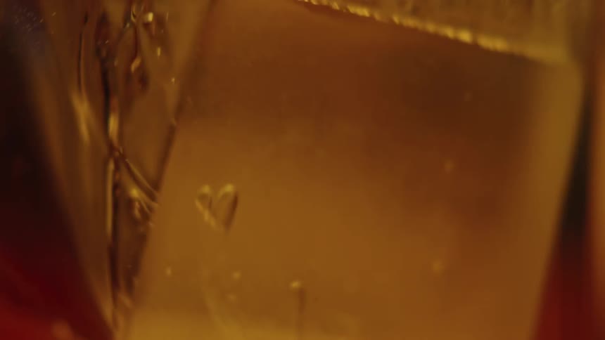 An ice cube falls and splashes into a glass of liquor