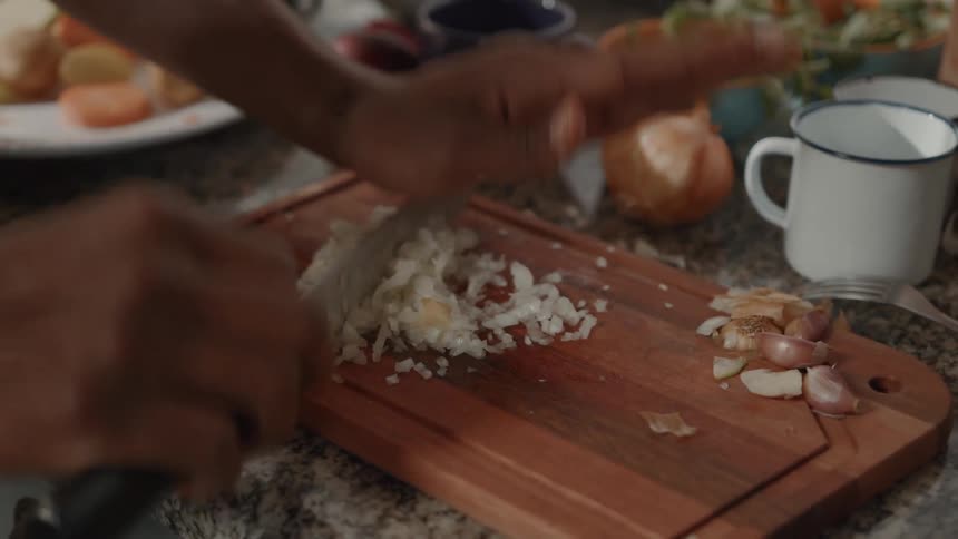 A persons hands skillfully mince garlic on a wooden cutting board in a kitchen