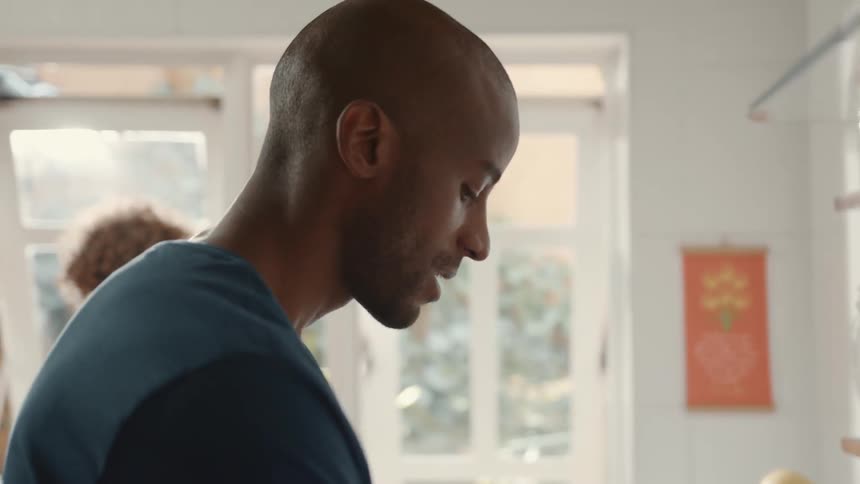 A man is cooking and singing in the kitchen with a woman standing beside him smiling