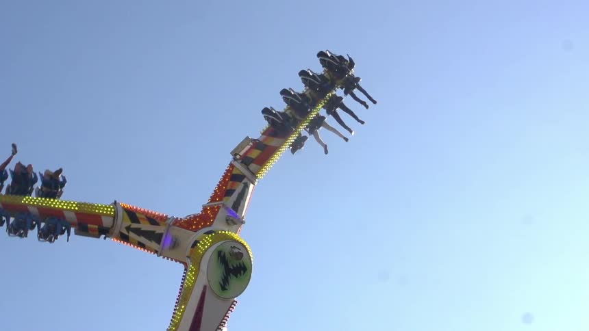 A lit amusement ride swinging people around on a sunny day